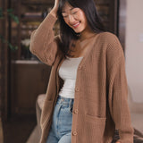 Modal smiling in a living room wearing Chunky Knit Women's Waffle Cardigan in Latte over white camisole and blue jeans