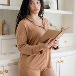 Woman in a beige outfit holding a book in a room with white shelves and cabinets.