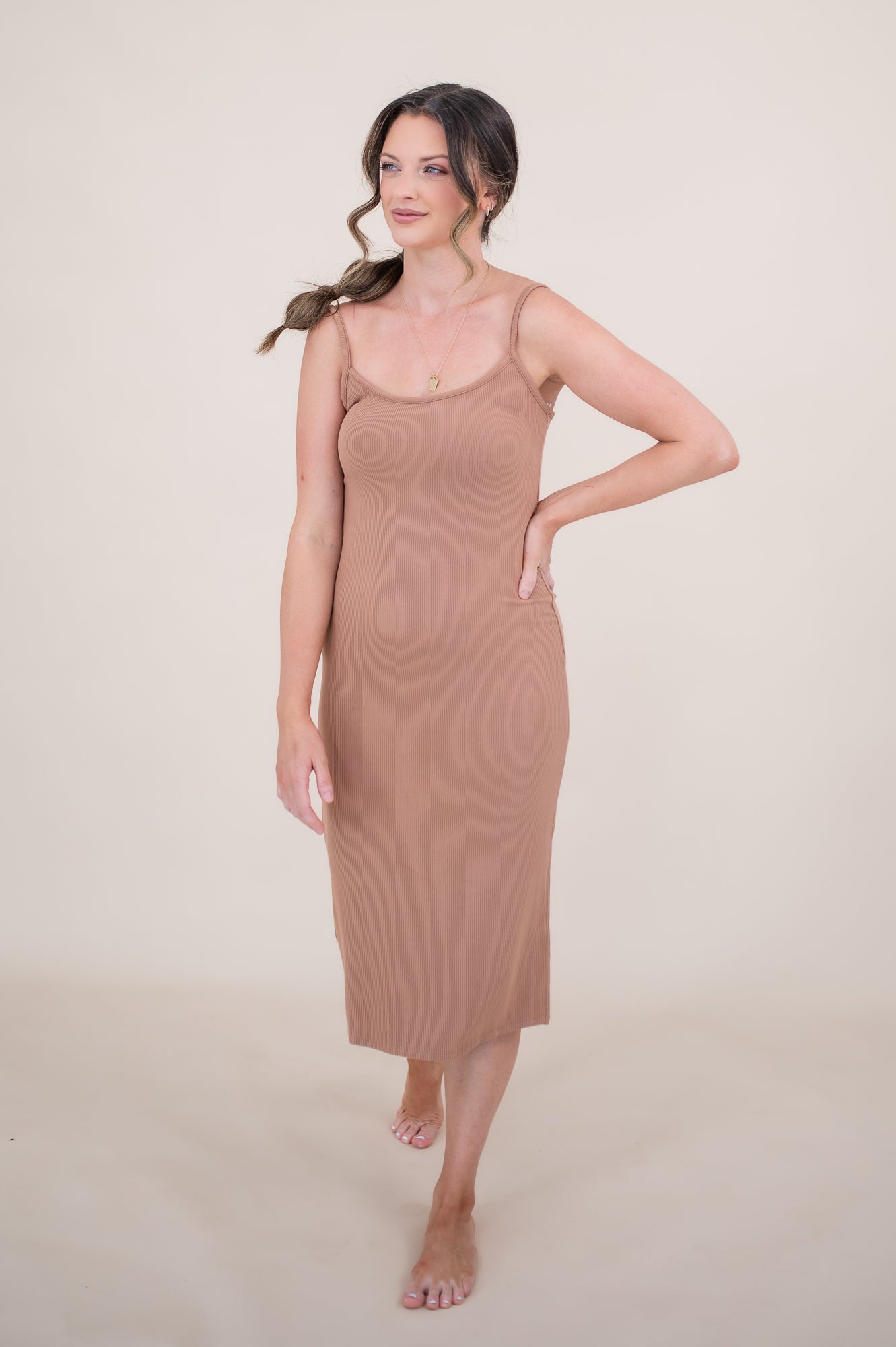 Woman looking to the side with one arm on hip while she models the  Ribbed Cami Dress in Latte