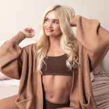 Woman wearing a light brown cardigan over a brown bralette on a neutral background