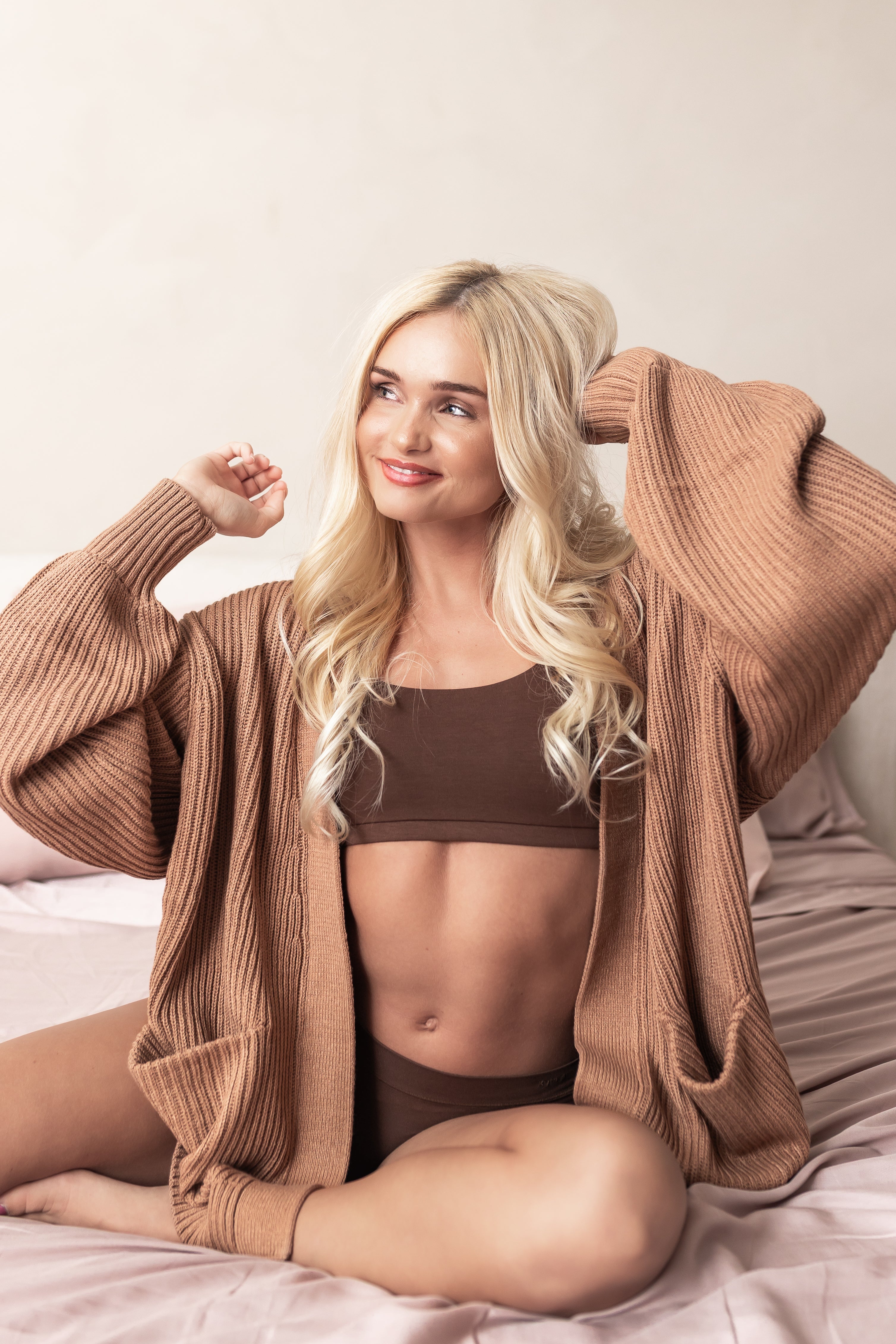 Woman wearing a light brown cardigan over a brown bralette on a neutral background