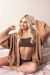 Woman wearing a light brown cardigan over a brown bralette on a neutral background