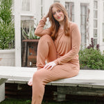 Woman sitting on a wooden bench wearing a bamboo matching set in a medium orange brown called Latte