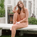 Woman sitting on a wooden bench wearing a bamboo matching set in a medium orange brown called Latte