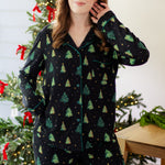 Woman in a black button up pj set with a christmas tree pattern in a festive holiday home setting