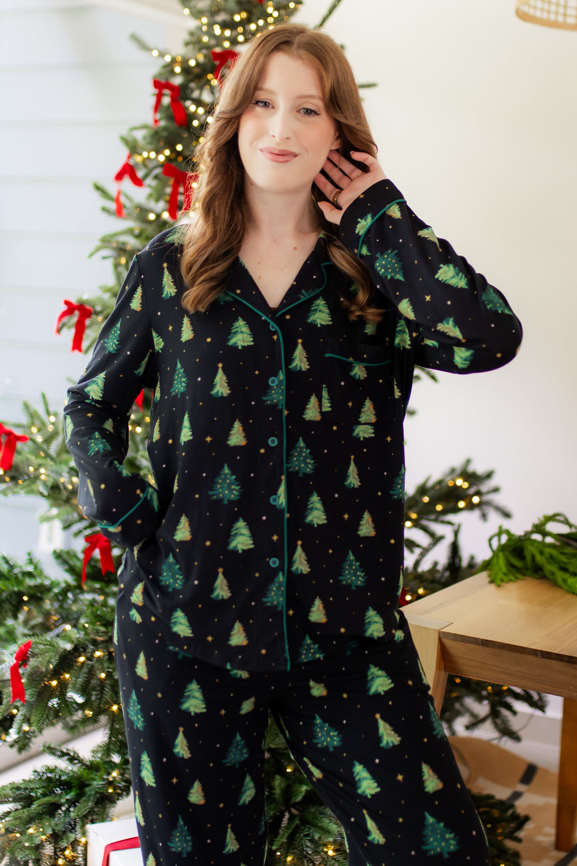 Woman in a black button up pj set with a christmas tree pattern in a festive holiday home setting