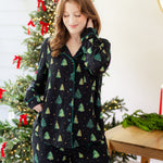 Woman in a black button up pj set with a christmas tree pattern in a festive holiday home setting