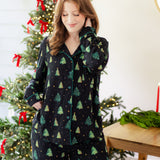 Woman in a black button up pj set with a christmas tree pattern in a festive holiday home setting