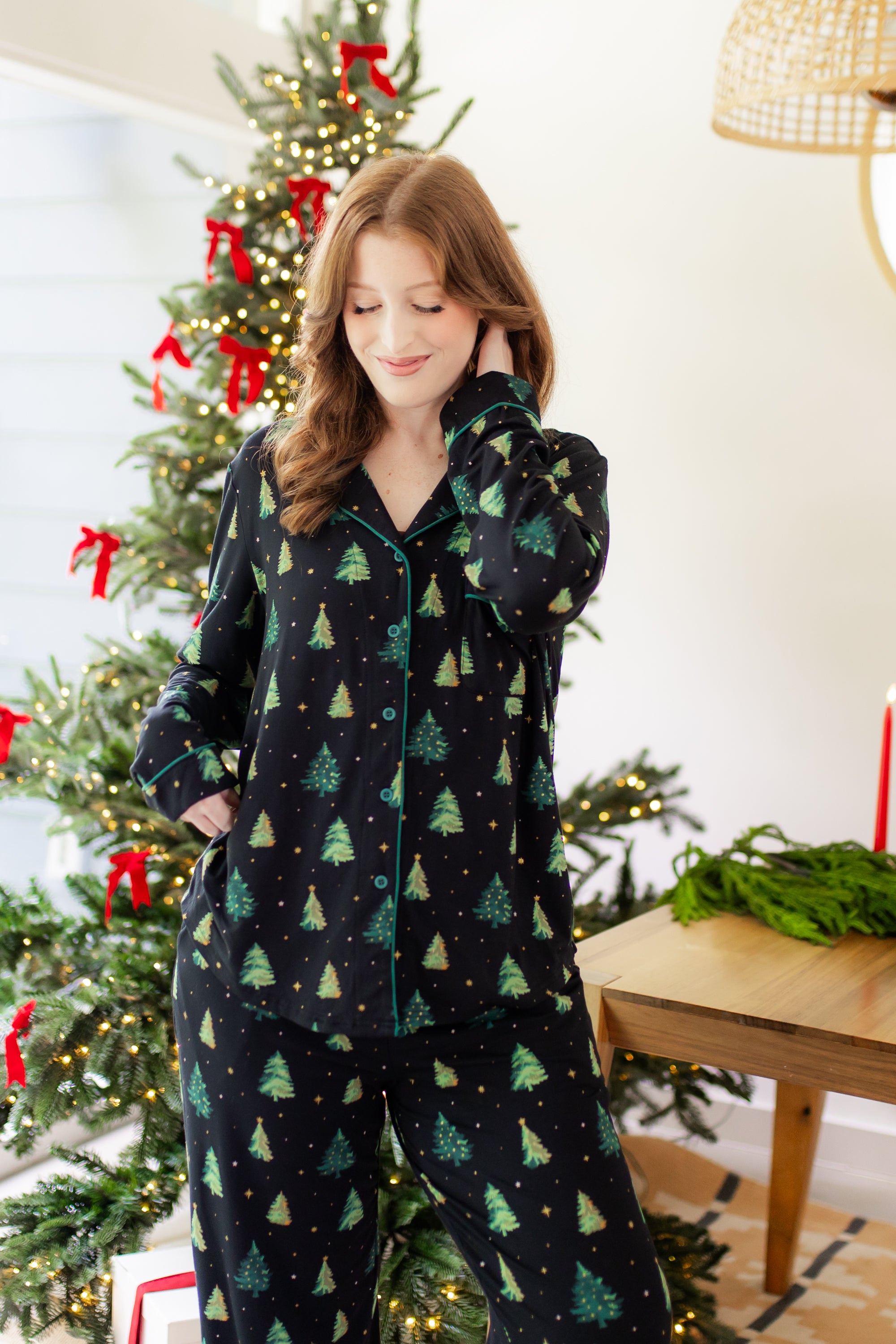Woman in a black button up pj set with a christmas tree pattern in a festive holiday home setting