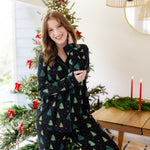 Woman in a black button up pj set with a christmas tree pattern in a festive holiday home setting