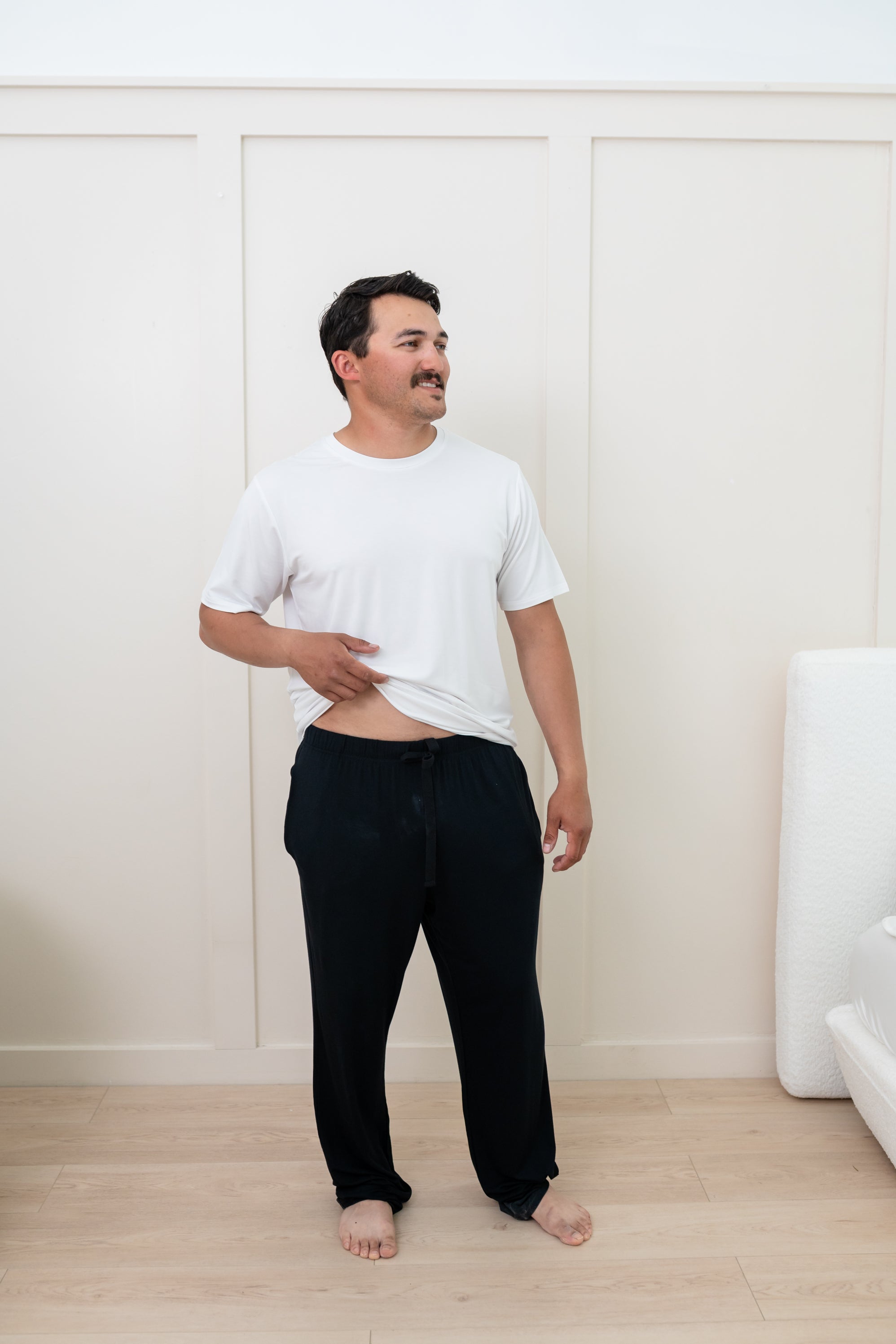 Man modeling Men's Lounge Pants in Midnight and Snow Crew Neck Tee. Slightly pulling up bottom of shirt to show the drawstring of pants.