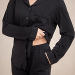 Female wearing the Long-Sleeved Women's Pajama Set in Midnight with Midnight Trim with one hand in the pants pocket and the shirt pulled up showing the elastic waistband