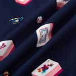 A close-up of navy blue fabric with a repeating print of Mahjong-style tiles in pink, white, and multicolor details, including floral motifs and playing card designs.
