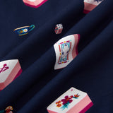 A close-up of navy blue fabric with a repeating print of Mahjong-style tiles in pink, white, and multicolor details, including floral motifs and playing card designs.