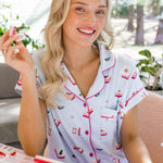 Woman in mahjong printed pajamas holding a mahjong tile, sitting at a table with pink and white items.