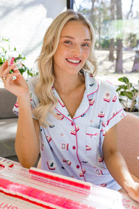 Woman in mahjong printed pajamas holding a mahjong tile, sitting at a table with pink and white items.