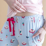 Light blue pajama pants with colorful Mahjong patterns and a pink bow, worn by a person.