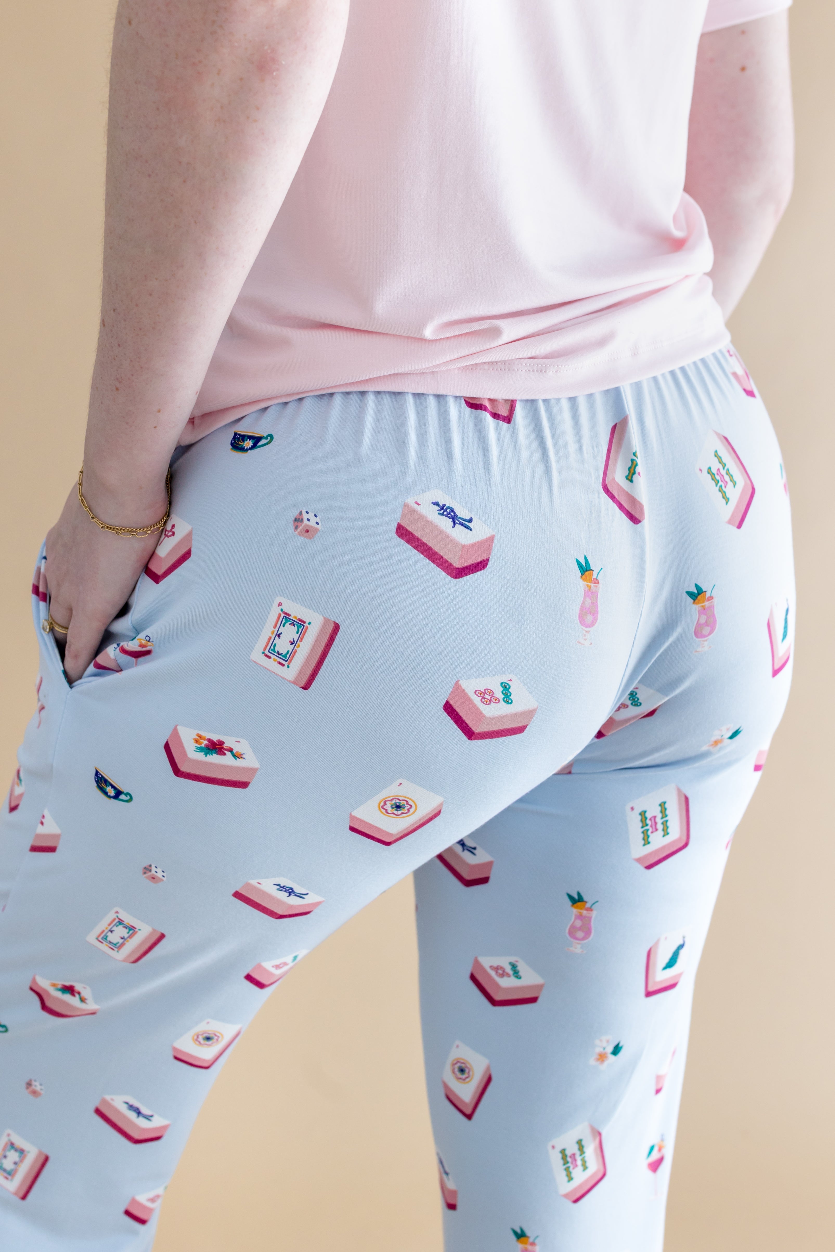 Light blue pajama pants with a pattern of Mahjong tiles and a pink shirt on a beige background