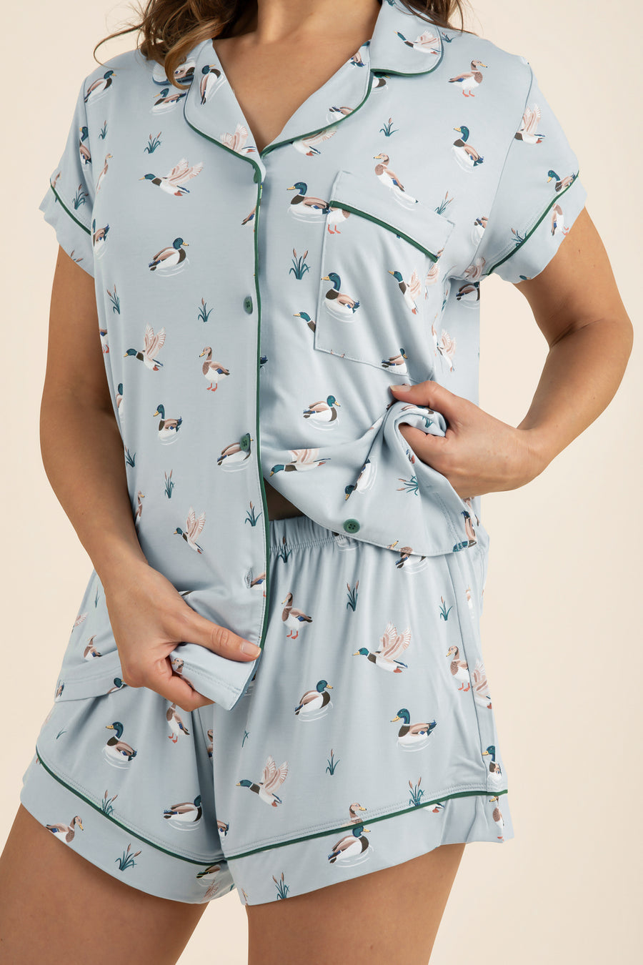 Light blue pajama set with duck pattern worn by a person on a beige 
background