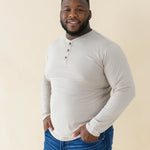 Male model wearing the Men's Long Sleeve Henley Top in Almond paired with medium wash jeans