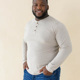Male model wearing the Men's Long Sleeve Henley Top in Almond paired with medium wash jeans