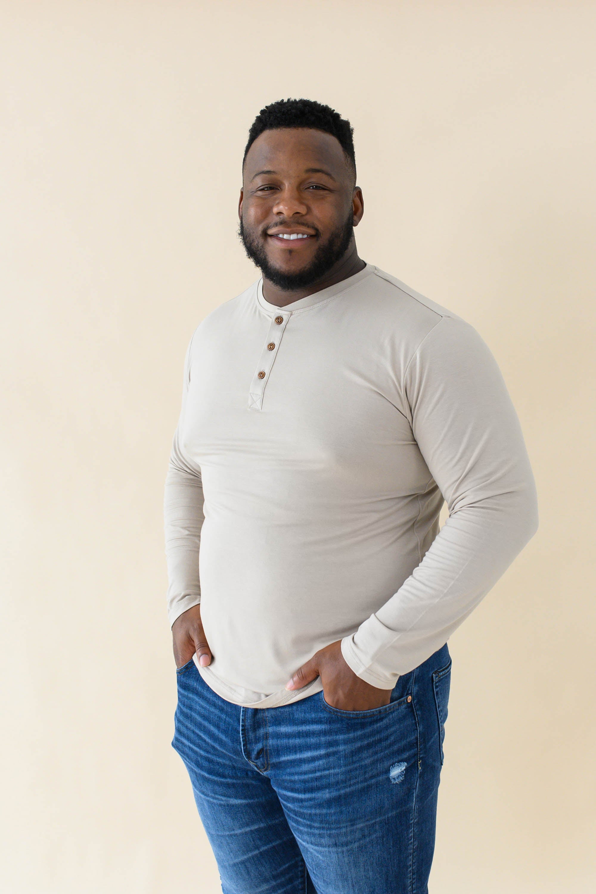Male model wearing the Men's Long Sleeve Henley Top in Almond paired with medium wash jeans