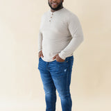 Male model wearing the Men's Long Sleeve Henley Top in Almond paired with medium wash jeans