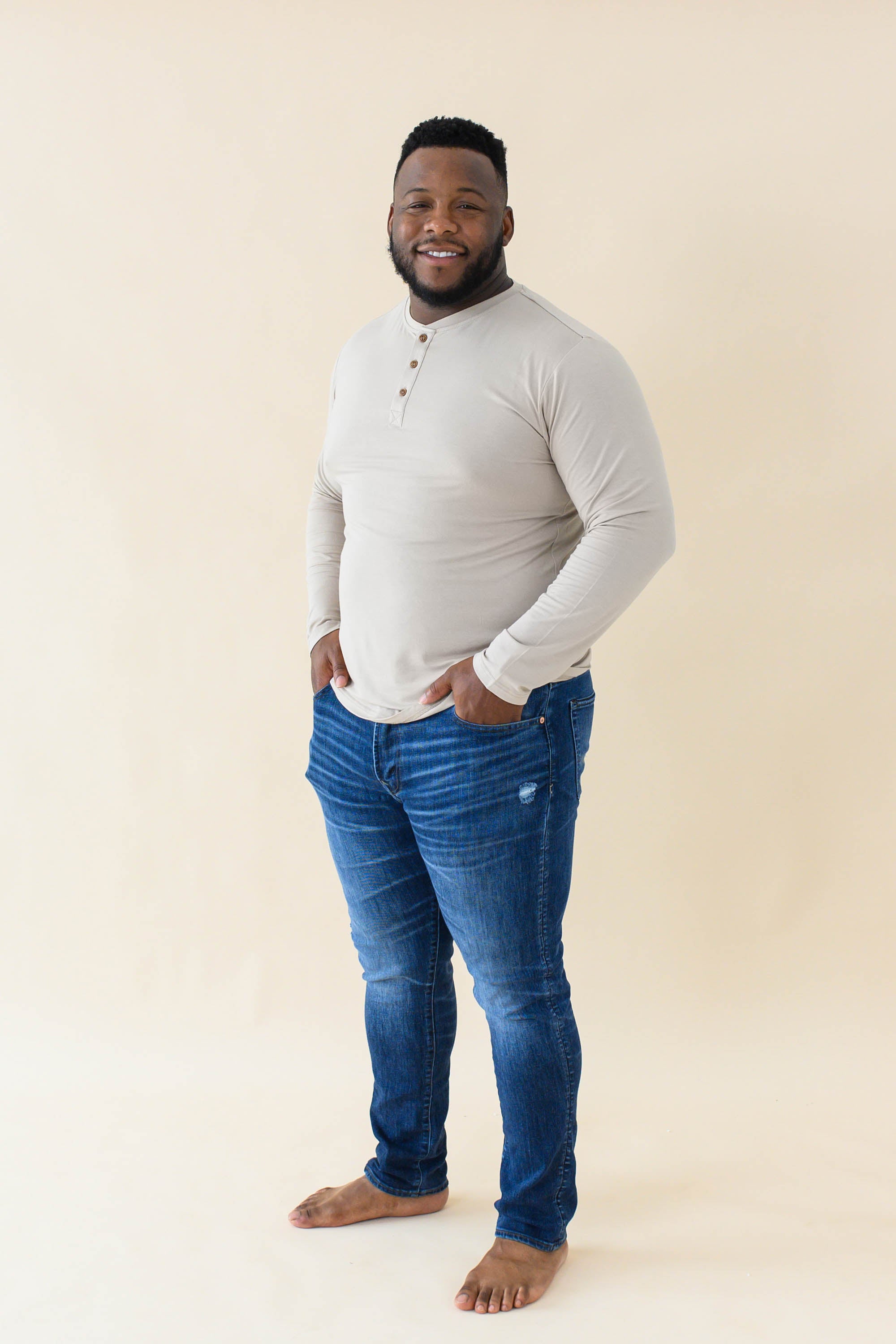 Male model wearing the Men's Long Sleeve Henley Top in Almond paired with medium wash jeans