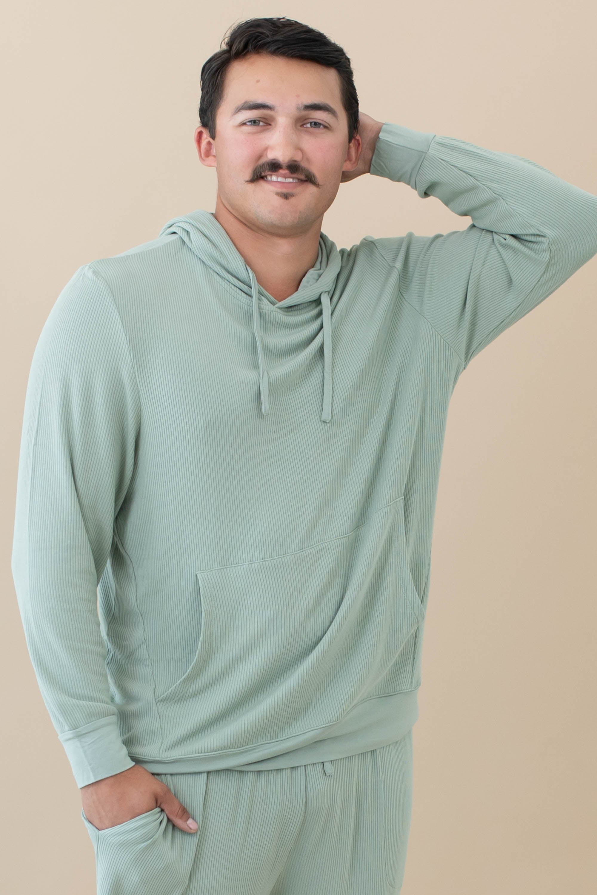 Male model wearing the Men's Ribbed Hoodie in Thyme with one arm up and behind his head