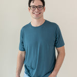 A smiling man in glasses wearing a Kyte Men's Crew Neck in Atlantic and light blue jeans