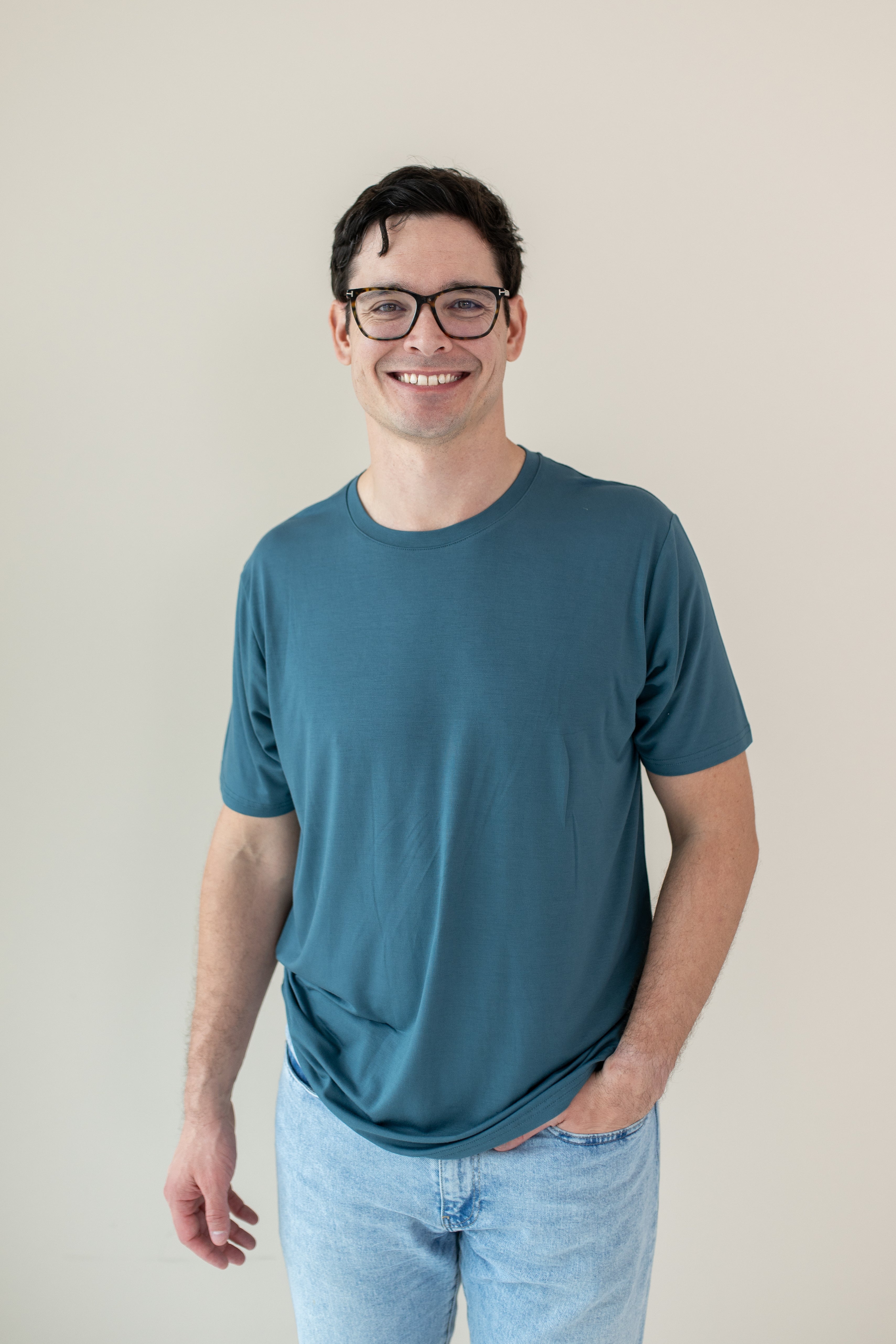 A smiling man in glasses wearing a Kyte Men's Crew Neck in Atlantic and light blue jeans