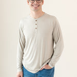 Model standing in an off-white room wearing Men's Long Sleeve Henley in Bisque and dark jeans with hand in pocket