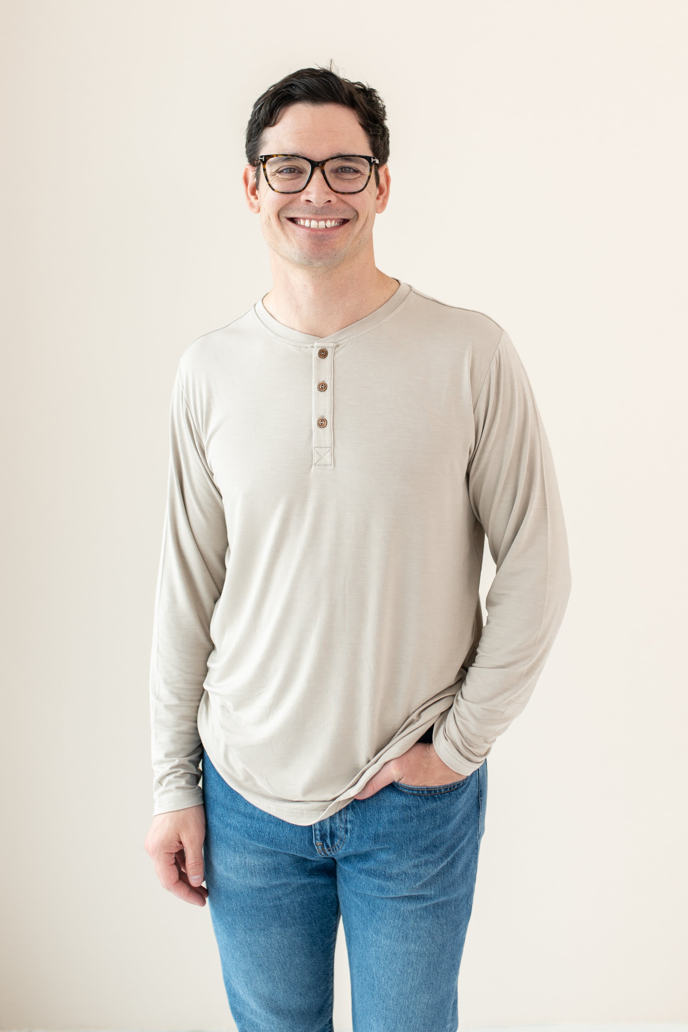 Model standing in an off-white room wearing Men's Long Sleeve Henley in Bisque and dark jeans with hand in pocket