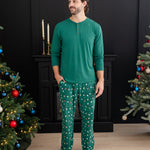 Male model looking off to the side standing with one hand in the pocket of the Men's Lounge Pants in Merry and Bright between two decorated Christmas Trees