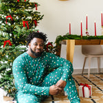 Male model sitting in front of a Christmas tree while wearing the Men's Jogger Set in Merry and Bright