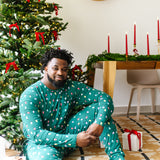 Male model sitting in front of a Christmas tree while wearing the Men's Jogger Set in Merry and Bright