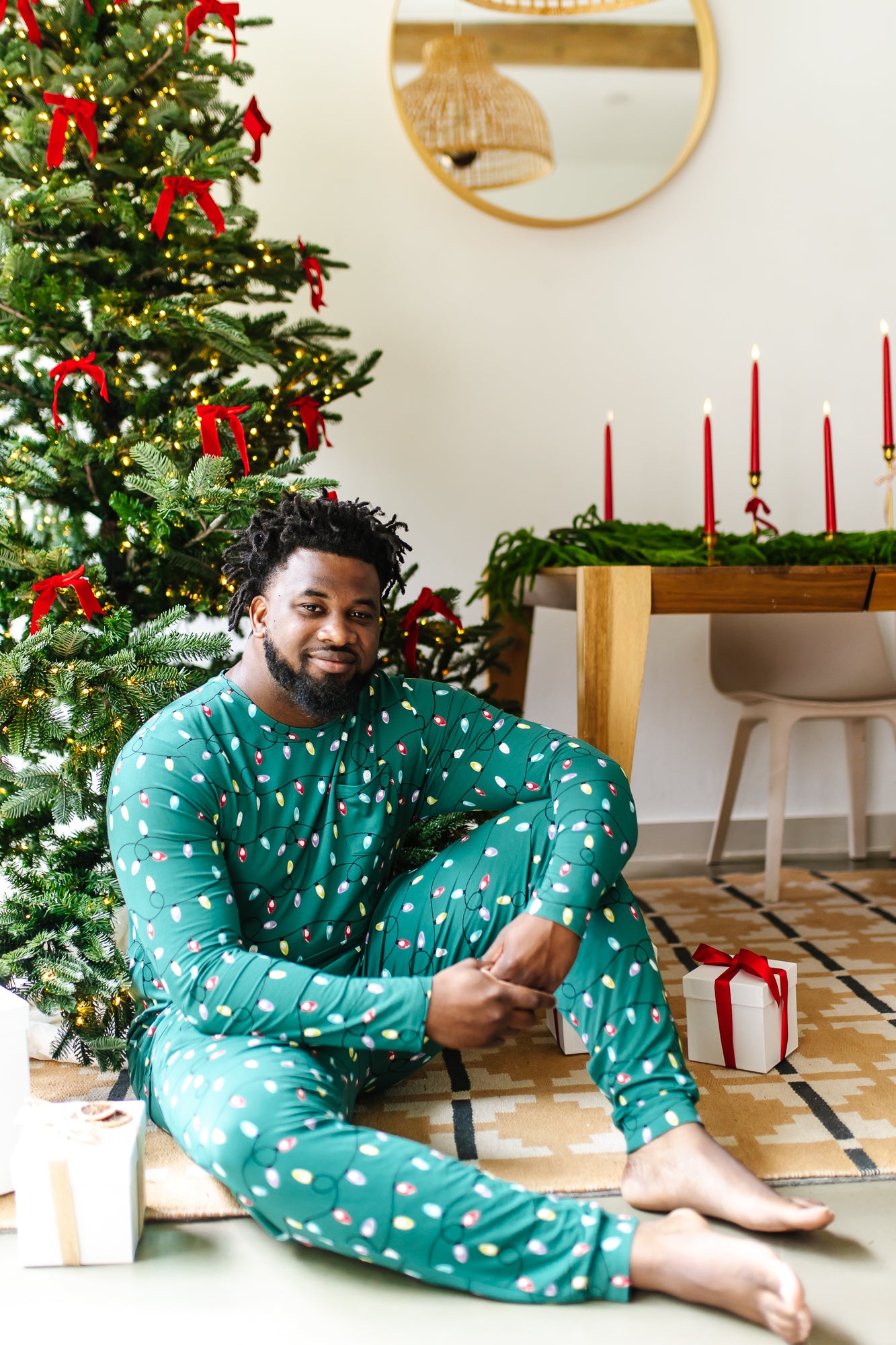 Male model sitting in front of a Christmas tree while wearing the Men's Jogger Set in Merry and Bright