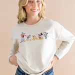 Smiling model wearing the Women's Sweatshirt in Mickey and Friends on Ecru with dark jeans