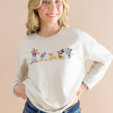 Smiling model wearing the Women's Sweatshirt in Mickey and Friends on Ecru with dark jeans
