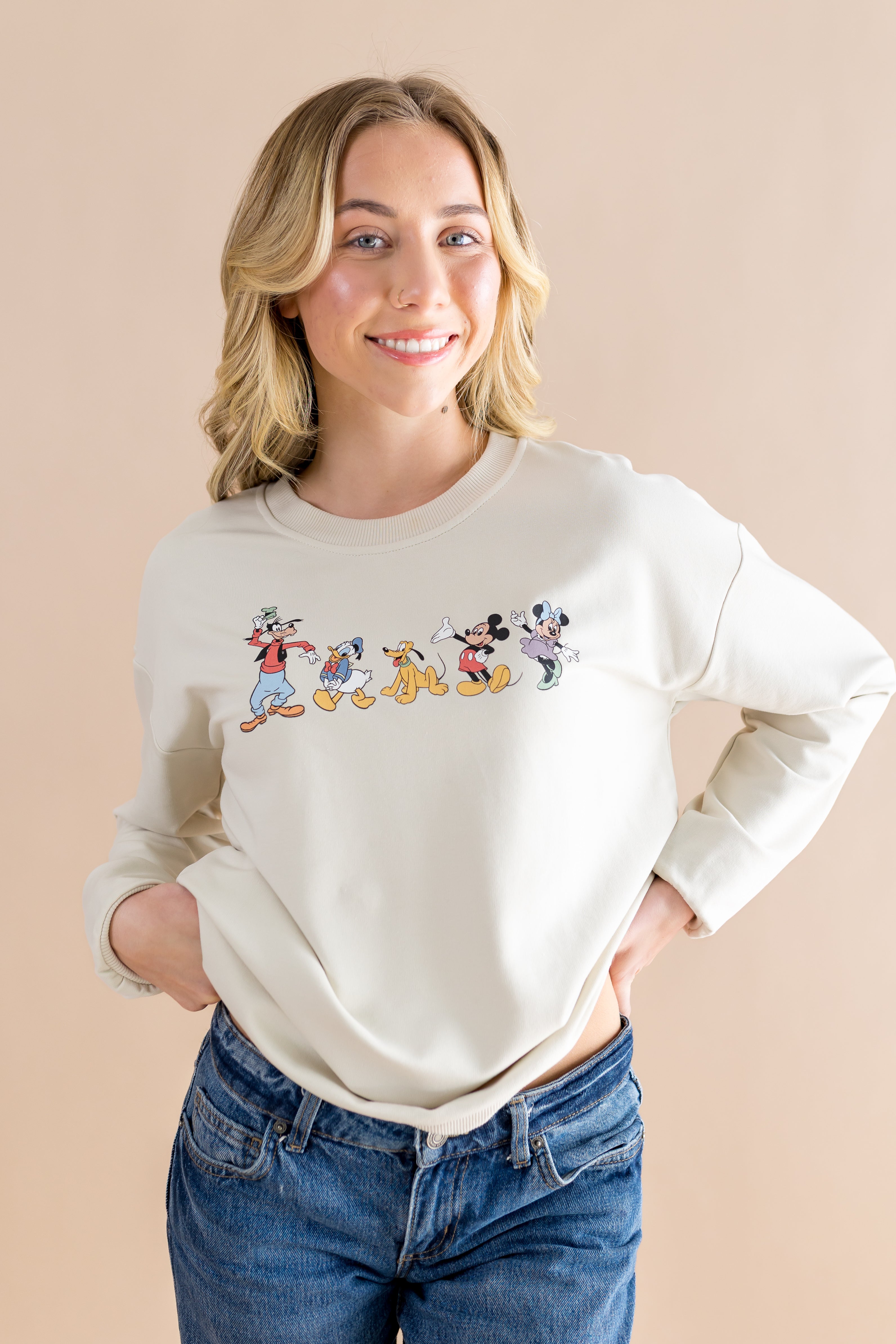 Smiling model wearing the Women's Sweatshirt in Mickey and Friends on Ecru with dark jeans