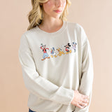 Woman standing in front of a beige back ground looking to the side while modeling the Women's Sweatshirt in Mickey and Friends on Ecru paired with dark wash jeans ::: Model is 5'7" wearing size S ///