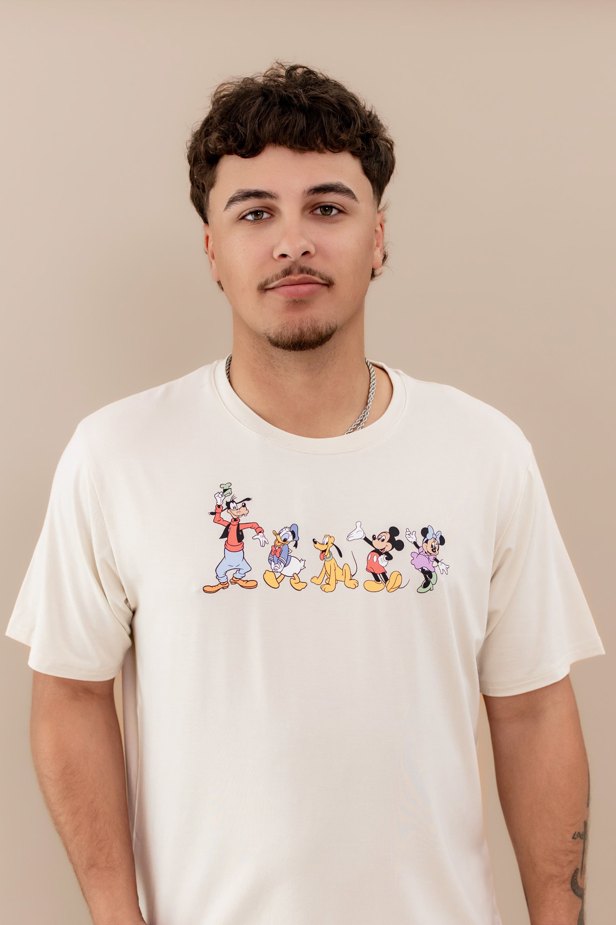 Close up of the Men's Crew Neck Tee in Mickey and Friends on Ecru on a male model standing in front of a beige background