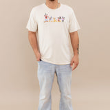 Male model wearing the Men's Crew Neck Tee in Mickey and Friends on Ecru paired with light wash jeans and white sneakers