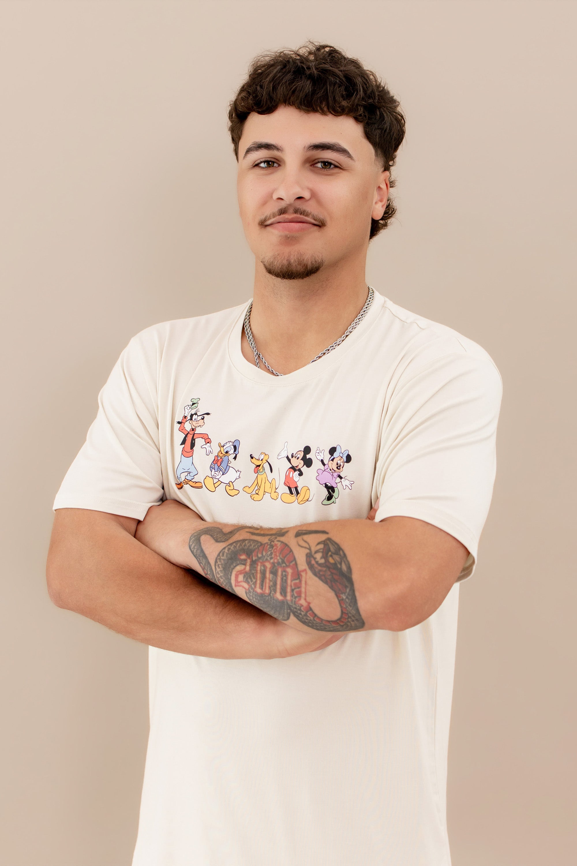Male model wearing the Men's Crew Neck Tee in Mickey and Friends on Ecru with his arms crossed in front of his chest