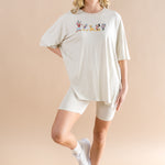 Smiling woman standing with one  leg folded up while modeling the Women’s Biker Short Set in Mickey and Friends on Ecru