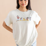 Model standing in front of a beige back ground while wearing the Women's Graphic Tee in Mickey and Friends on Ecru with her hands behind her back paired with jean shorts

::: Model is 5' wearing size XS ///
