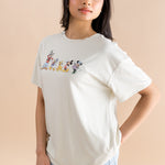 Model standing to the side while wearing the Women's Graphic Tee in Mickey and Friends on Ecru paired with light wash denim shorts