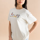 Model standing to the side while wearing the Women's Graphic Tee in Mickey and Friends on Ecru paired with light wash denim shorts