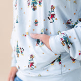 Woman showcasing pockets on Women's Hoodie in Mickey & Friends Christmas print on blue jeans on a beige background