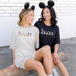 2 women wearing biker short sets in a cream and black colorway with mickey and friend graphic and wearing mickey mouse ear headbands